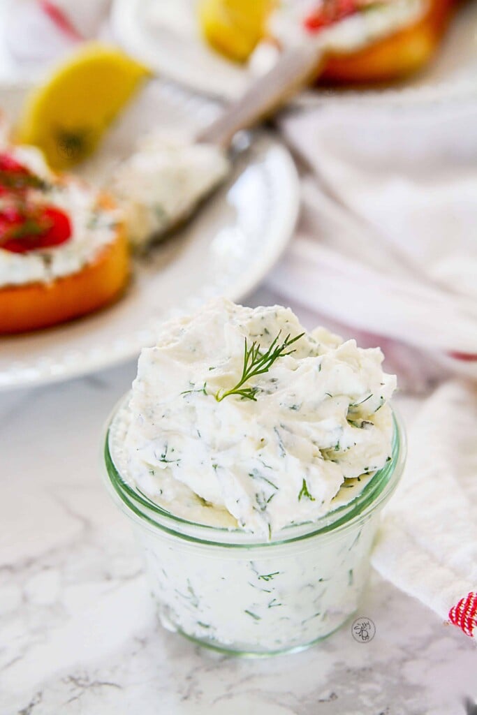 Lemon Dill Yogurt Cream cheese in a small glass jar with tomato cream cheese toast in the background.