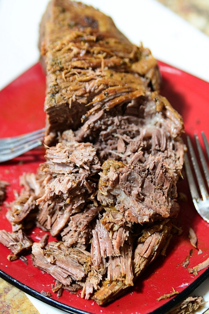 Shredded roast beef sitting on a red plate after being pressure cooked.