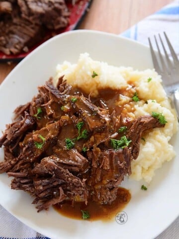 3 packet roast beef with gravy on mashed potatoes on a white plate.