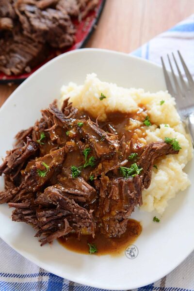 3 packet roast beef with gravy on mashed potatoes on a white plate.