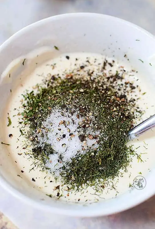 a white bowl with white creamy dressing and dried dill with salt and pepper on top.