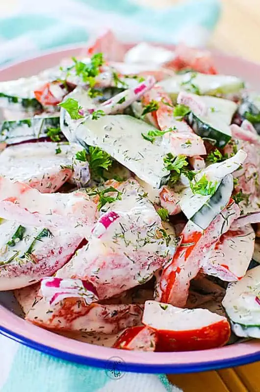 A close image of the cucumber salad. Cucumbers, tomatoes and red onions all covered in dressing.