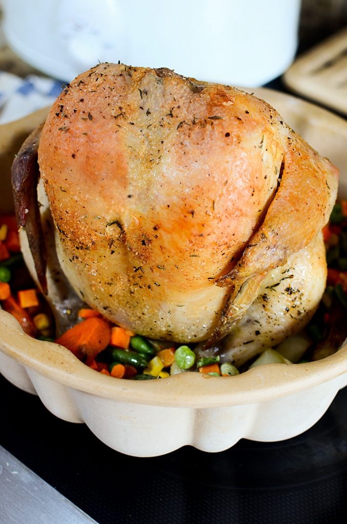 A whole roasted chicken atop a bundt pan with veggies around it.