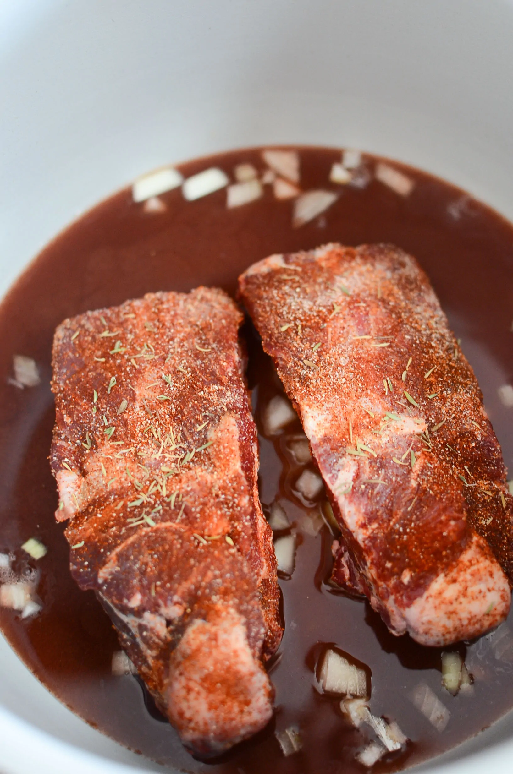 Two raw and seasoned beef short ribs resting in cooking liquids in the ninja foodi.
