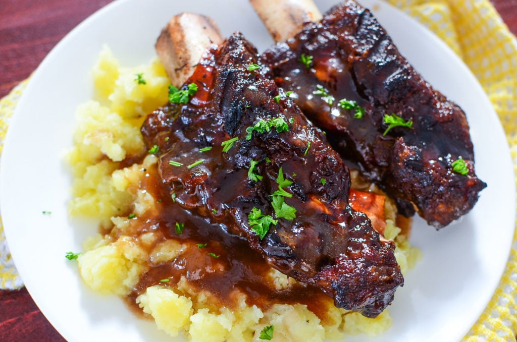 Saucy bbq short ribs on a bed of mashed spuds on a white plate with a yellow napkin