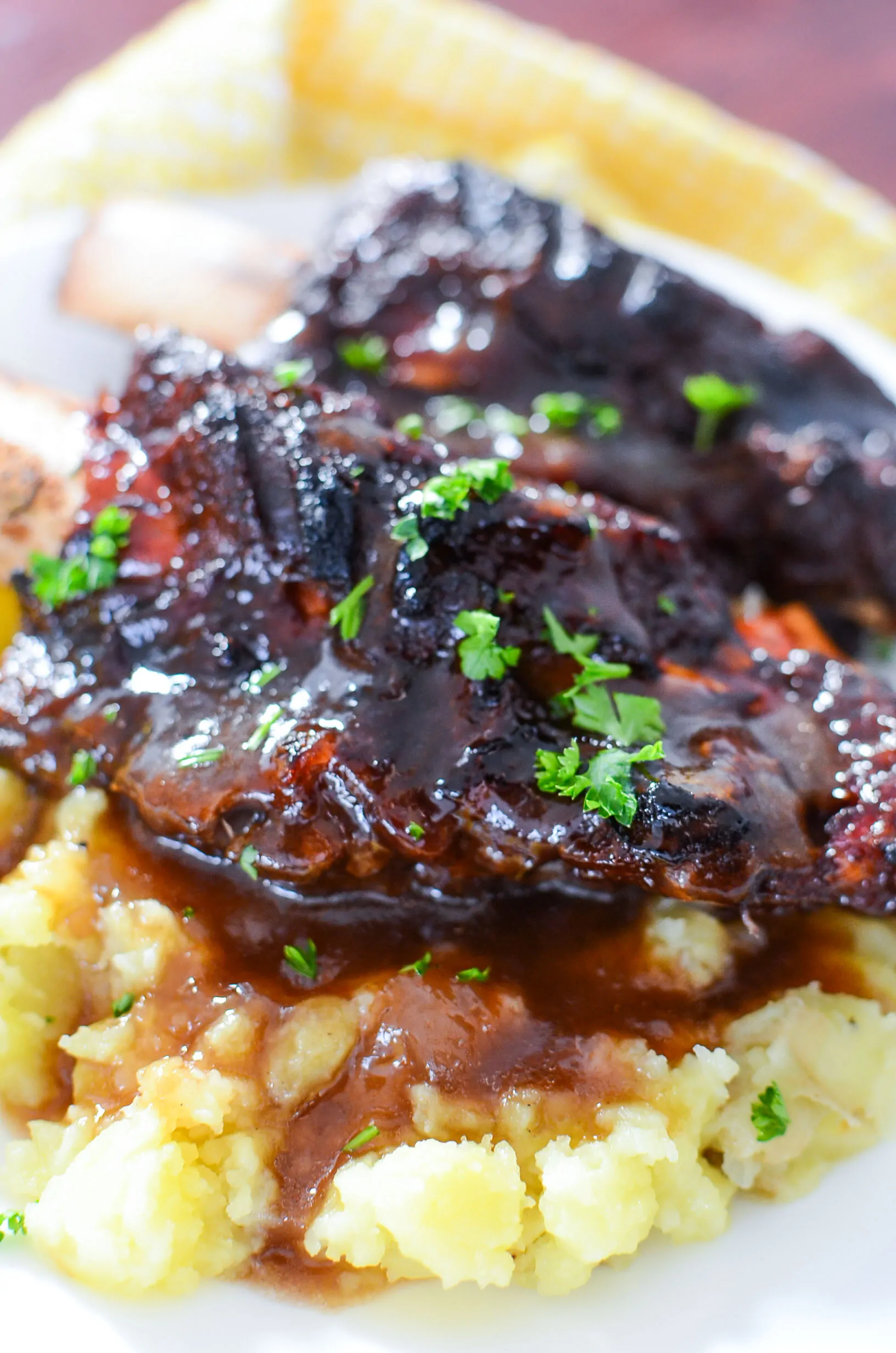 A super close up photo of cooked beef short ribs nestled in mashed potatoes with bbq gravy on a white plate