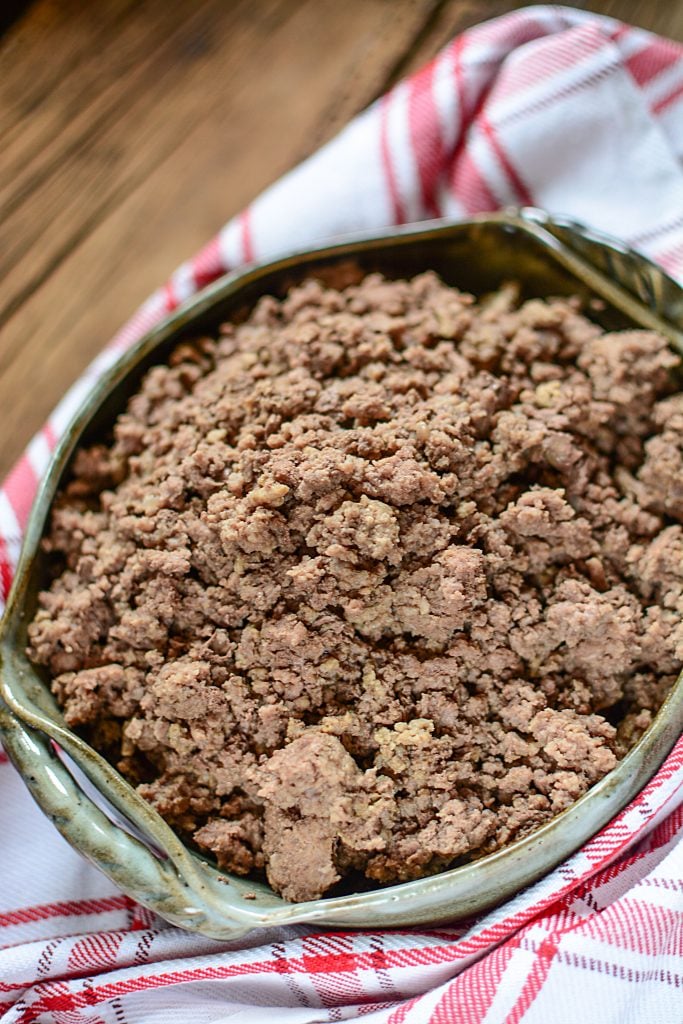 Cooked ground beef on a red checked napkin inside a green serving dish.