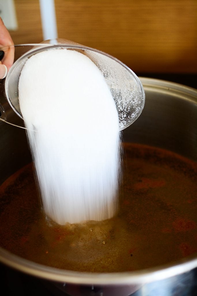 pouring the sugar into a pot that is making the pickle brine