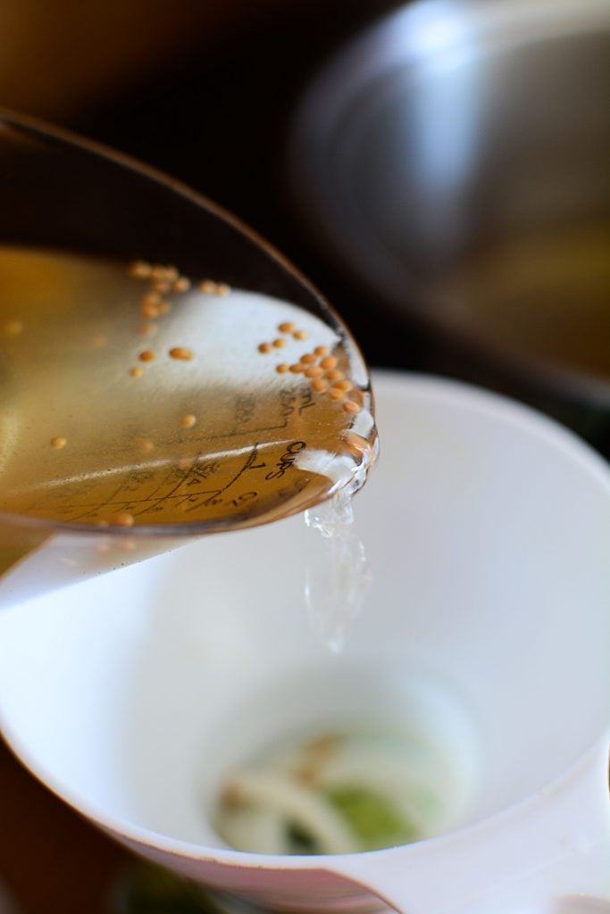 The pickle brine going into a funnel inside the mason jar.