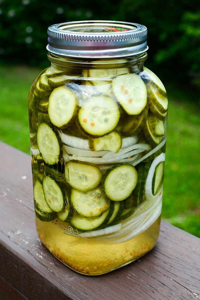 a close up photo of the cucumbers and onions in the brine inside a mason jar