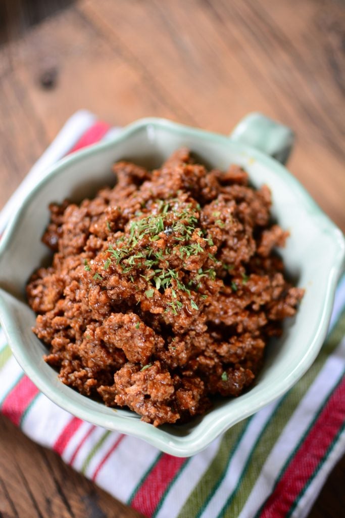 This delicious taco meat is piled high in a pretty green bowl sitting on a colorful napkin.