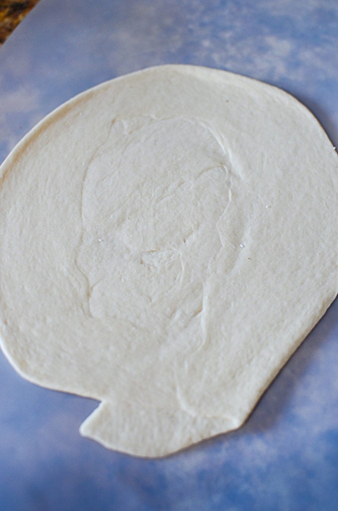 The dough rolled out into a circle, sitting on a cutting mat. 