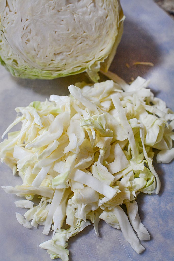A photo of shredded cabbage with the rest of the head of cabbage in the background