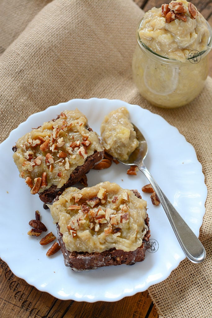 Instant pot maple banana butter on chocolate scones with pecans on top, on a white plate with a jar of the spread in the background.