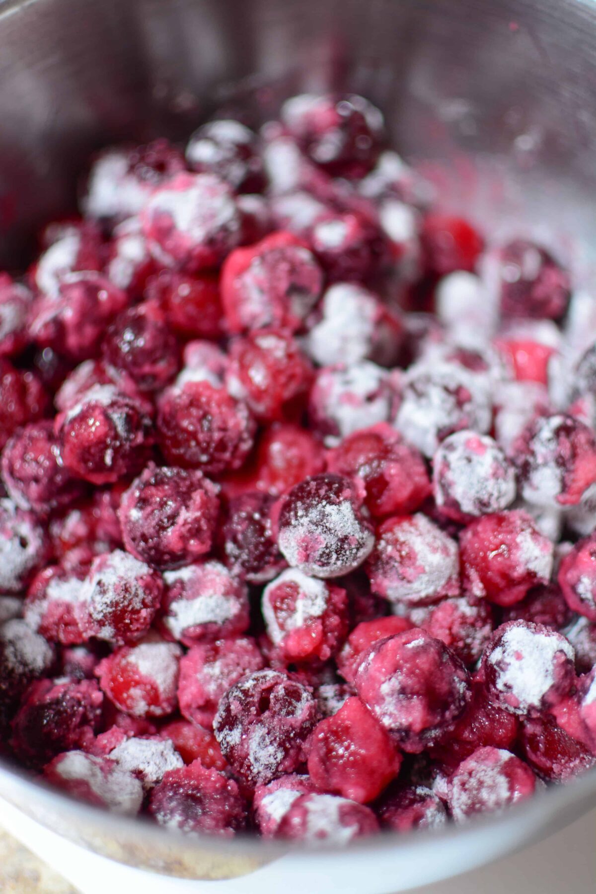 Sour cherries covered in flour and sugar in a bowl.