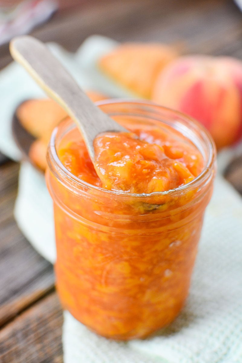 Peach jam in a mason jar with a spoon sticking out the top. 