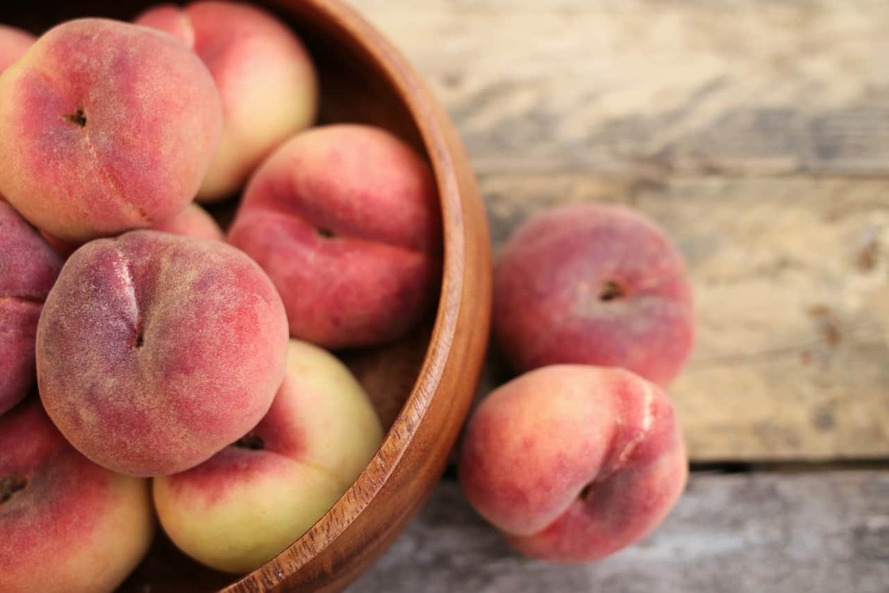 Peaches in a wooden bowl on a wooden table.