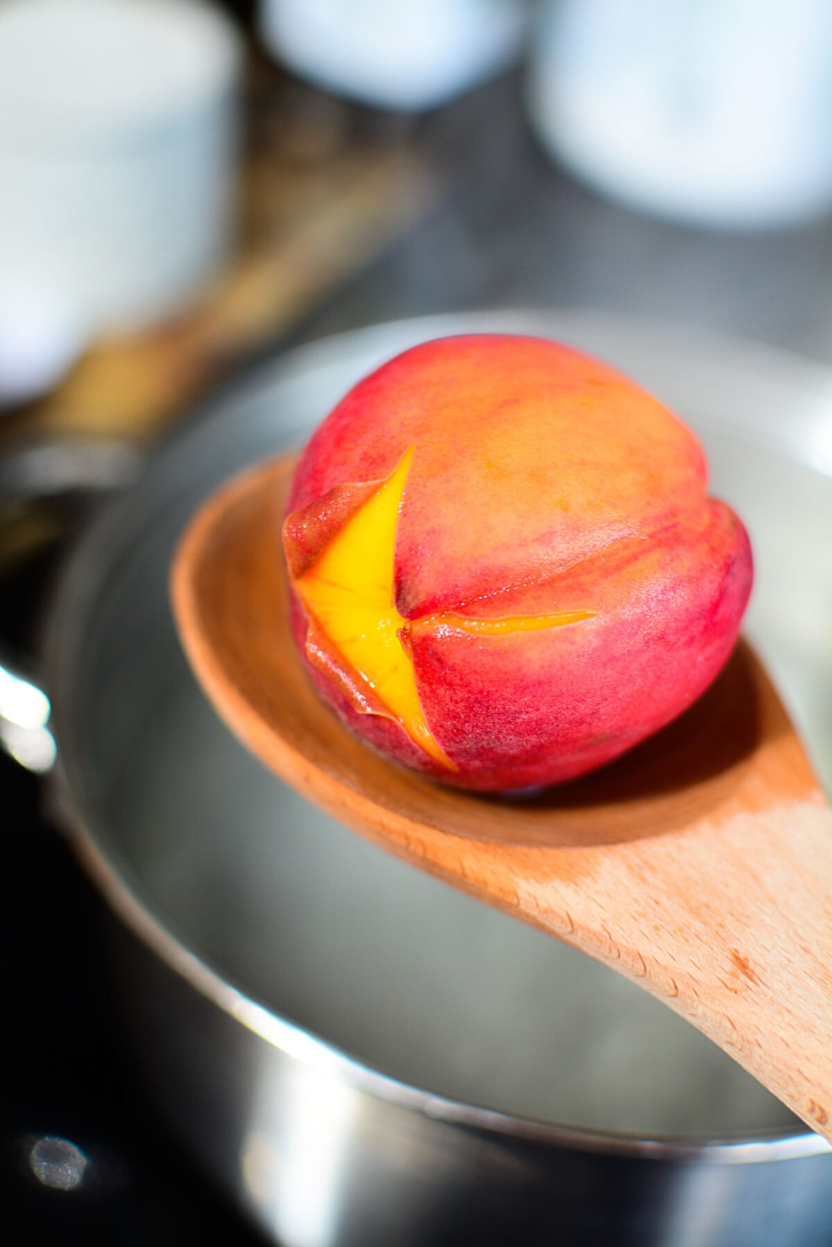 The peel beginning to come away from the peach while resting on a wooden spoon.