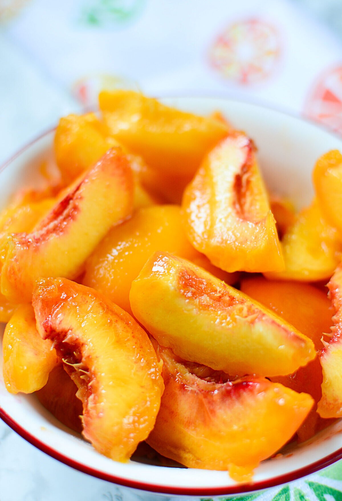 Cut and peeled peaches in a white bowl with a patterened napkin.