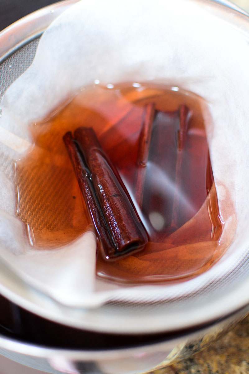 Cinnamon sticks inside a coffee filter, straining liquid.