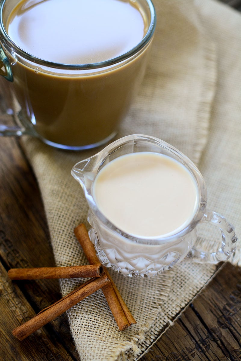 A cup of coffee sits at the top left with a small glass pitcher with creamer in it, sits in the center of the photo. 