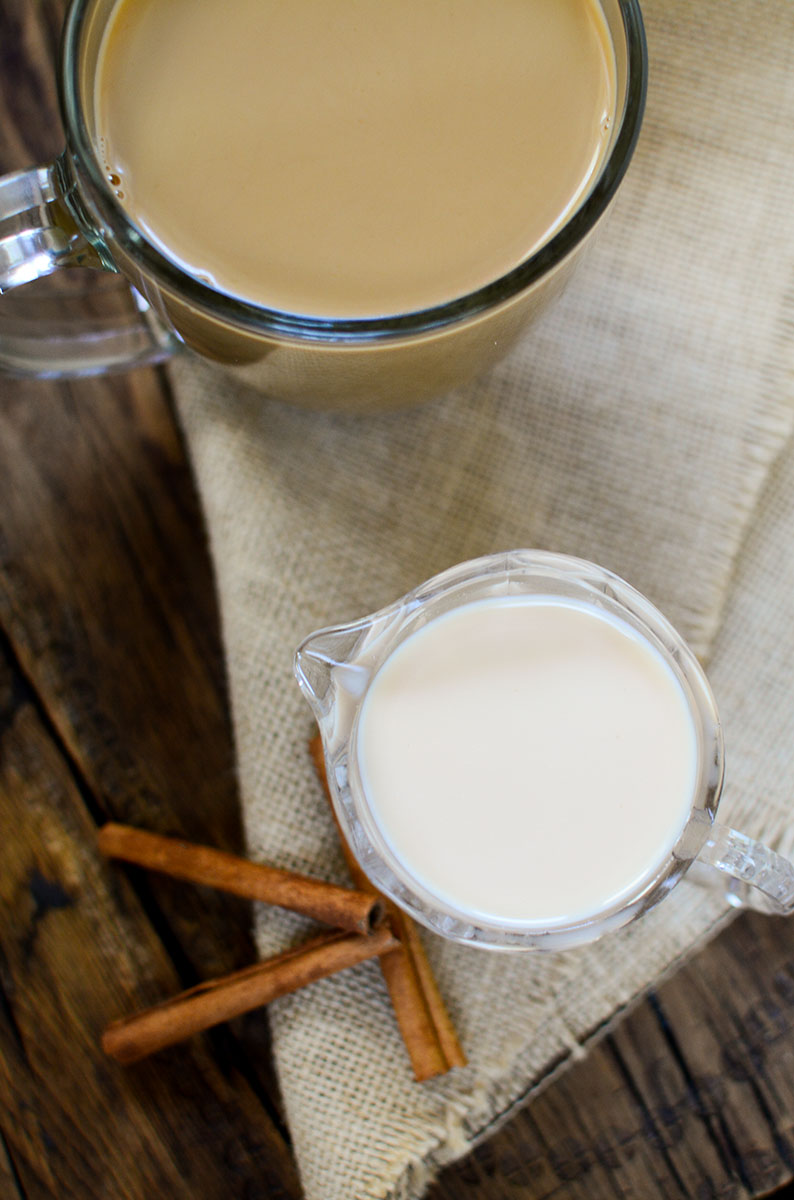 An overhead image of a cup of coffee at the top left and coffee creamer in a crystal decanter in the center of the photo.