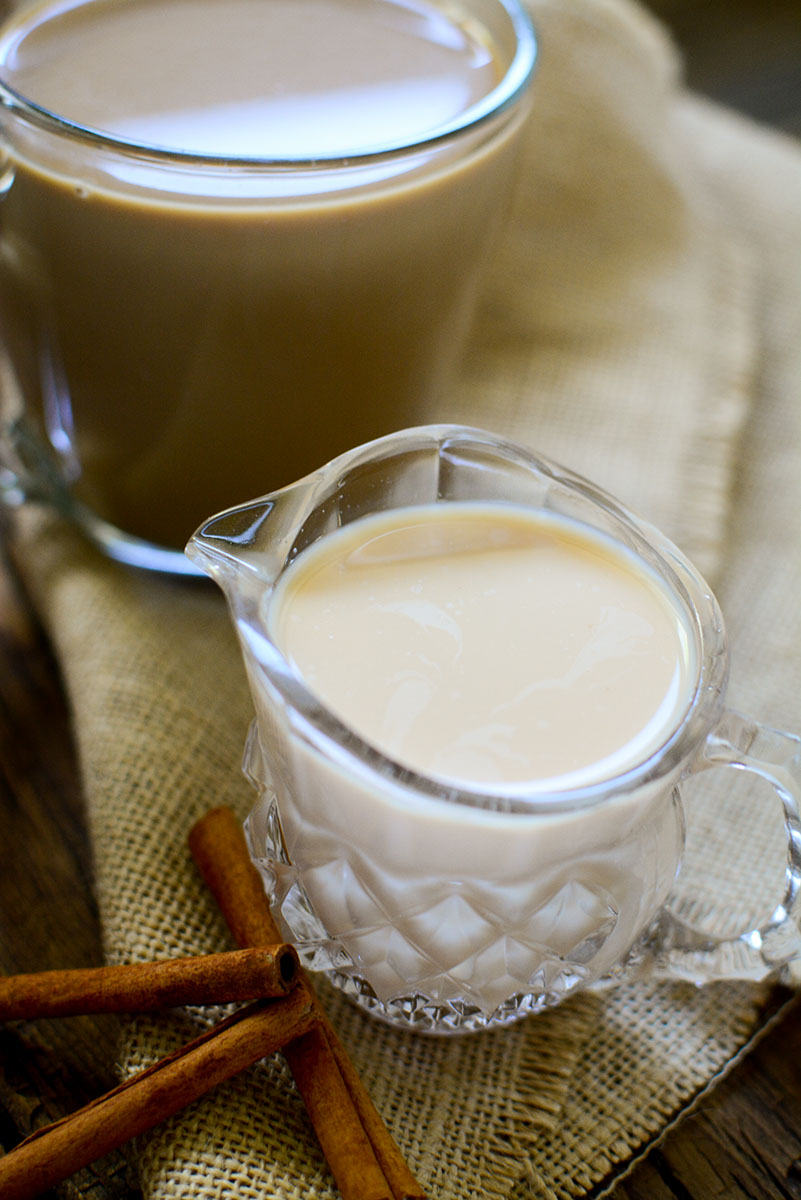 A glass creamer jar sitting on burlap with 3 cinnamon sticks next to it.