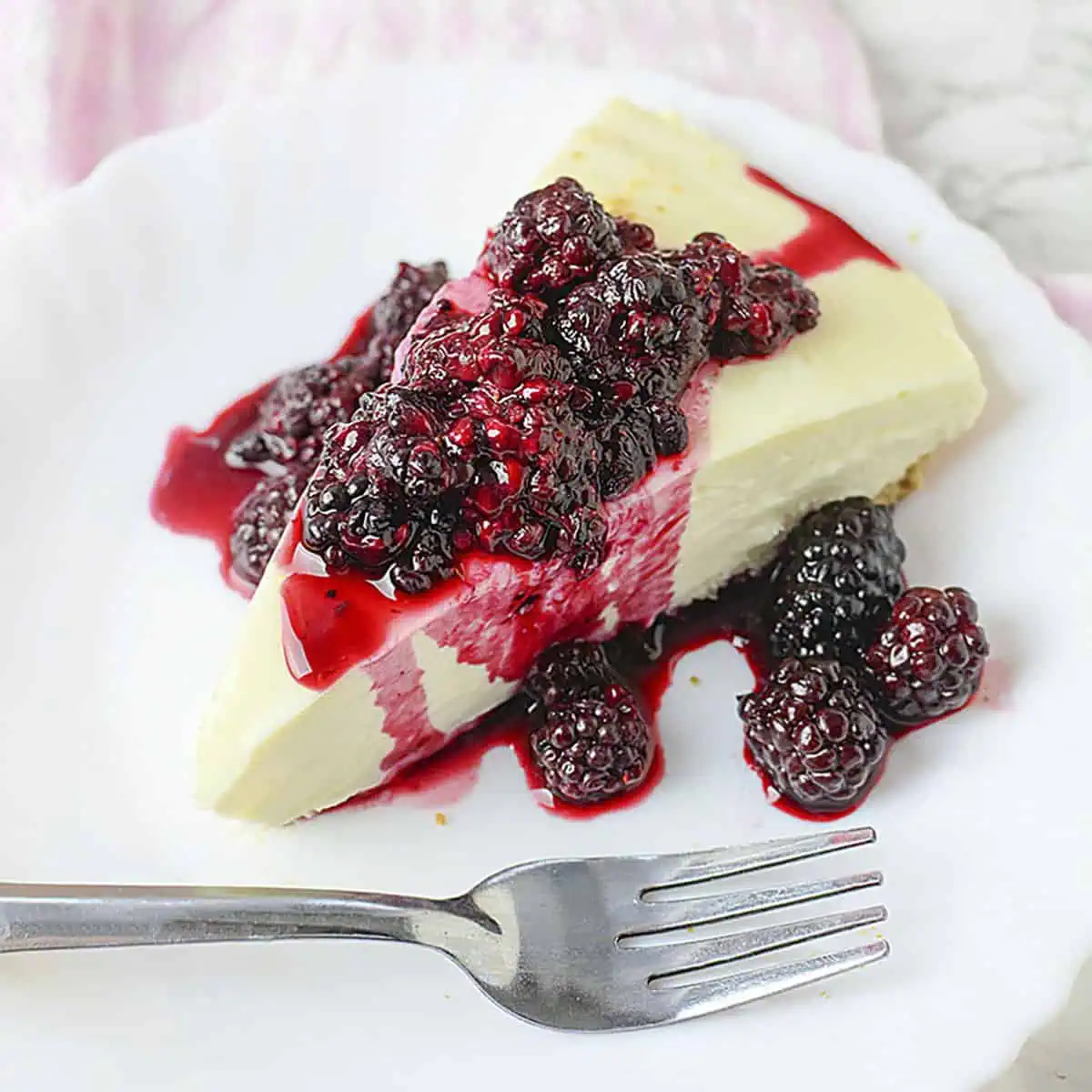 3 Ingredient cheesecake with blackberry topping on a white plate with a fork.