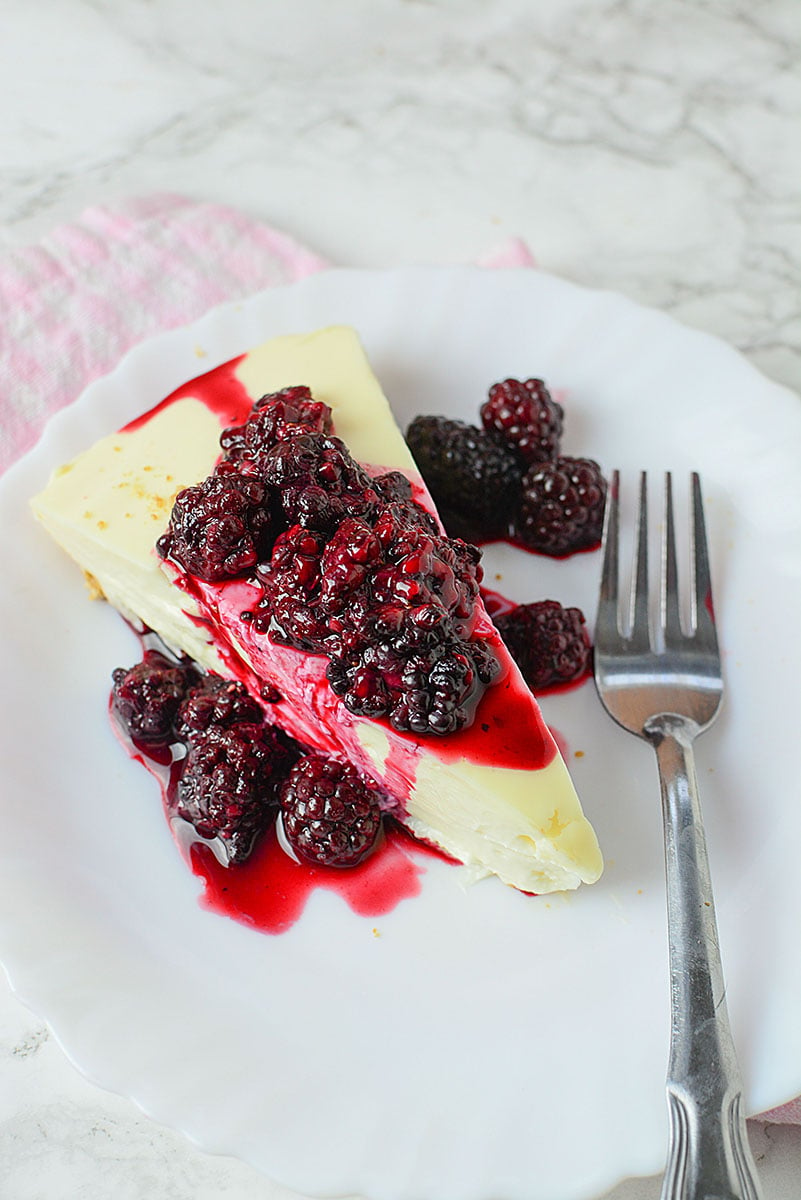 A slice of cheesecake with blackberries and a fork on a white plate.