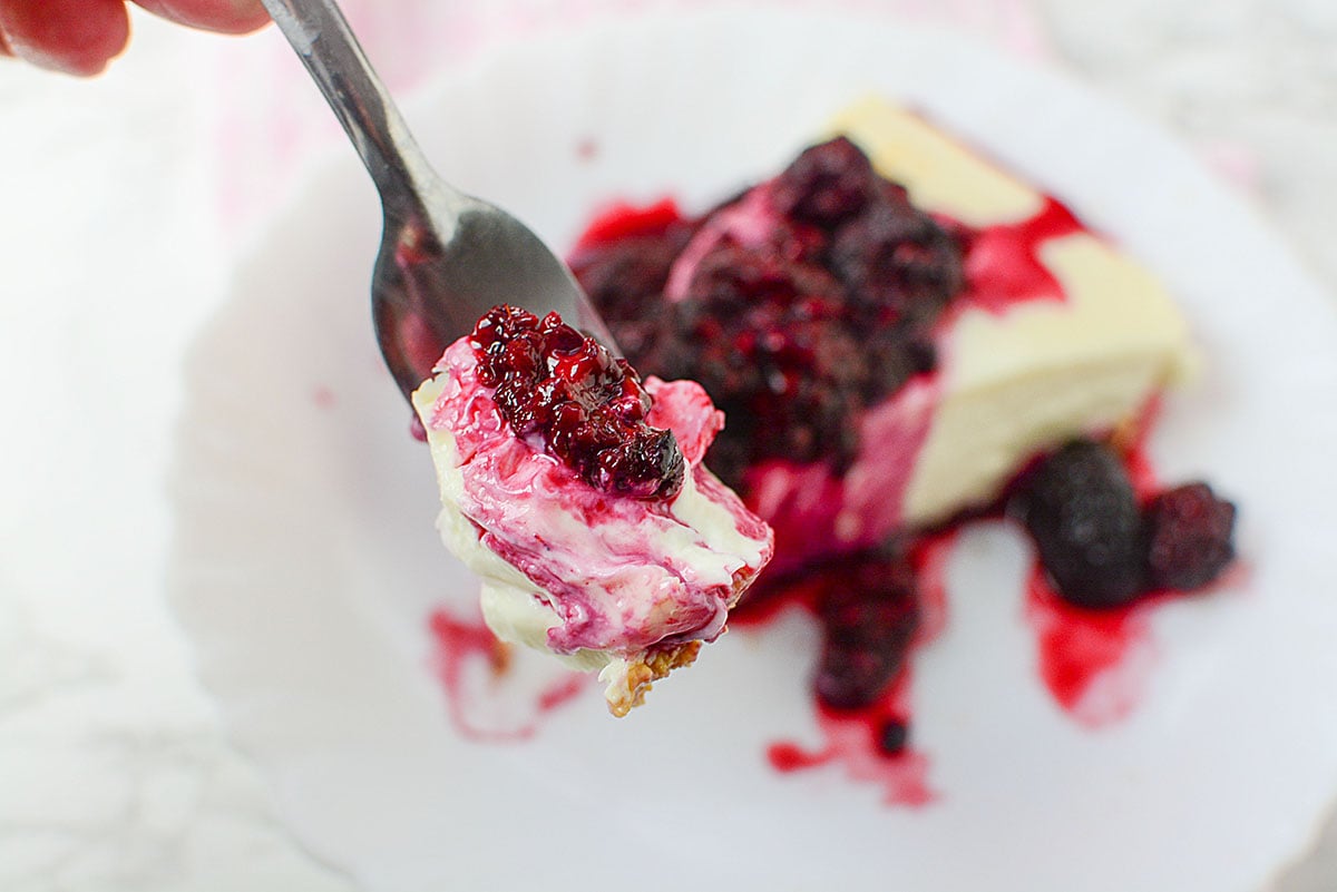 A forkfull of cheesecake with blackberry topping.