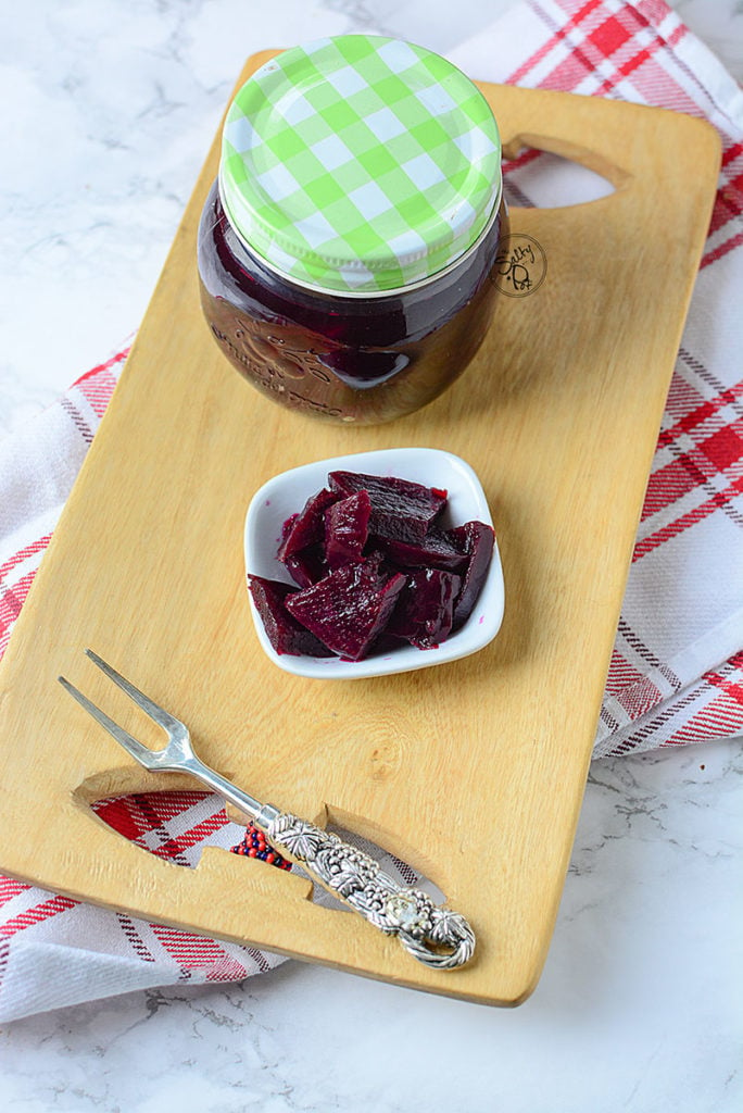 A small amount of beet pickles sitting on a white plate with a jar of the beets beside it. 