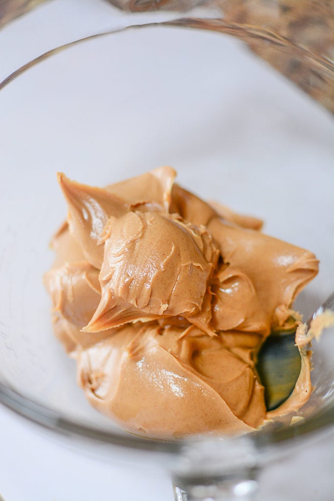 An up close image of some peanut butter on a spoon laid on a transparent bowl