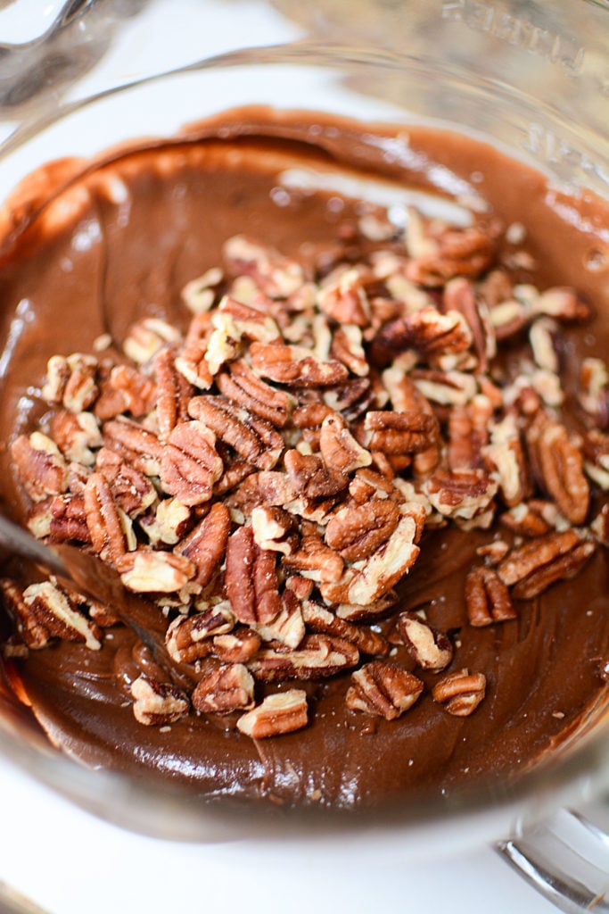 A mixture of some peanut butter and chocolate frosting , and pecans, in a bowl