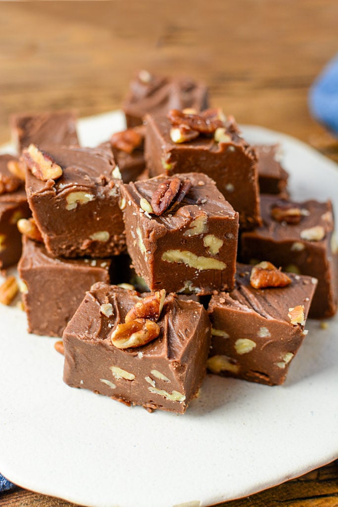 een afbeelding van ongeveer 15 blokken chocolade fudge met noten, zittend op een witte plaat.