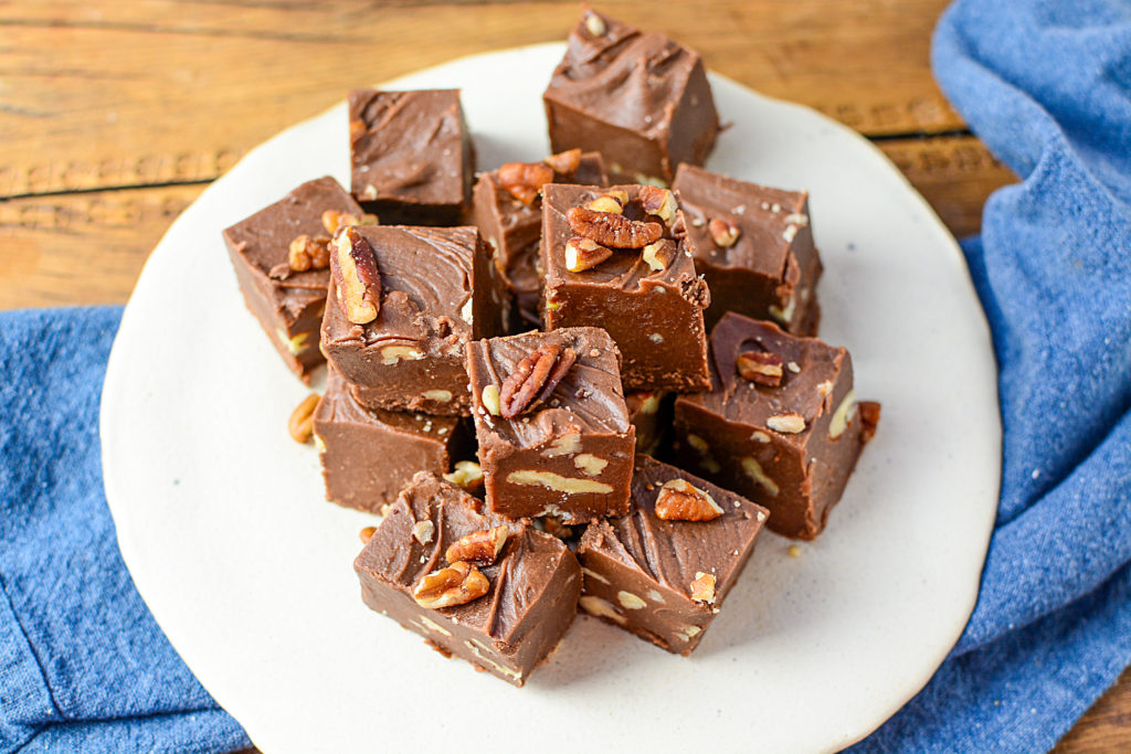 An image of blocks of chocolate fudge with nuts, sitting on a white plate with blue cloth under the plate.
