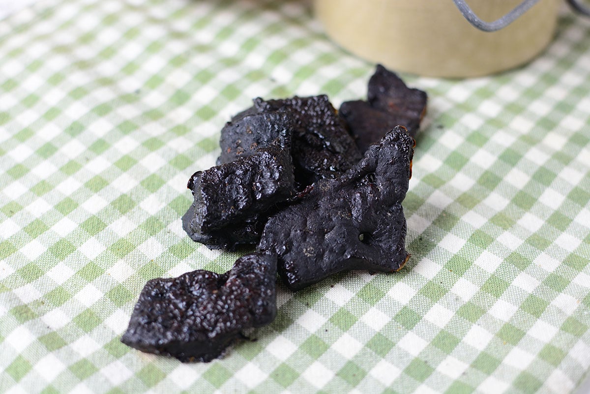 A picture of seven pieces of homemade liver dog treats sitting on a green and white checkered table cloth. 