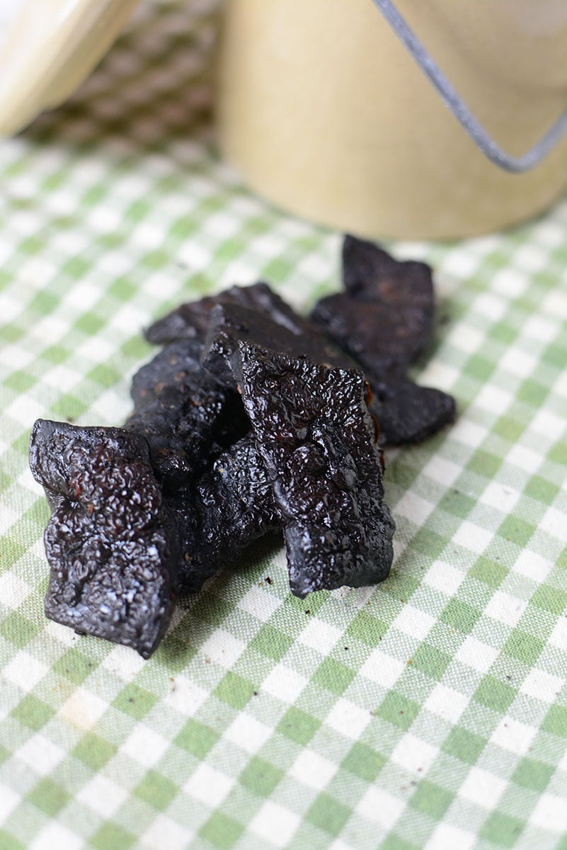 A picture of seven pieces of homemade liver dog treats sitting on a green and white checkered table cloth. 