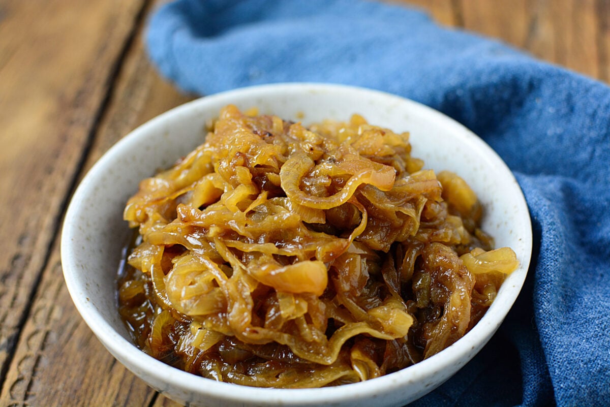 Caramelized onions in a white bowl with a blue napkin on the right.