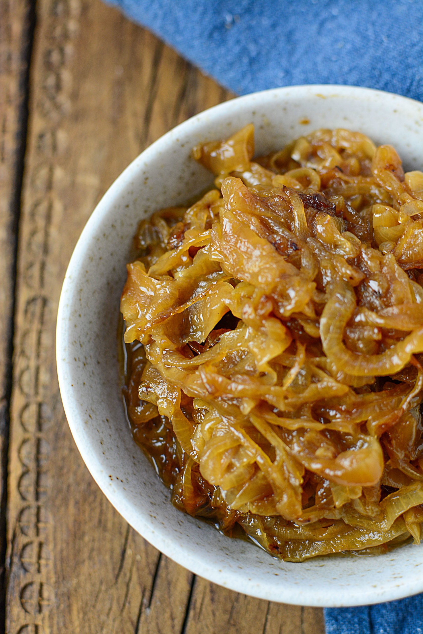 A white bowl with browned onions on a wooden backdrop.