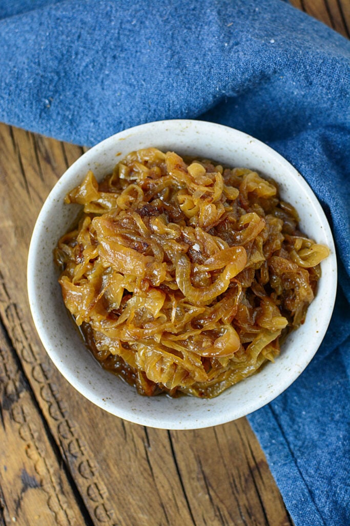 Onions that have been caramelized. They are sitting in a bowl on a wooden background.