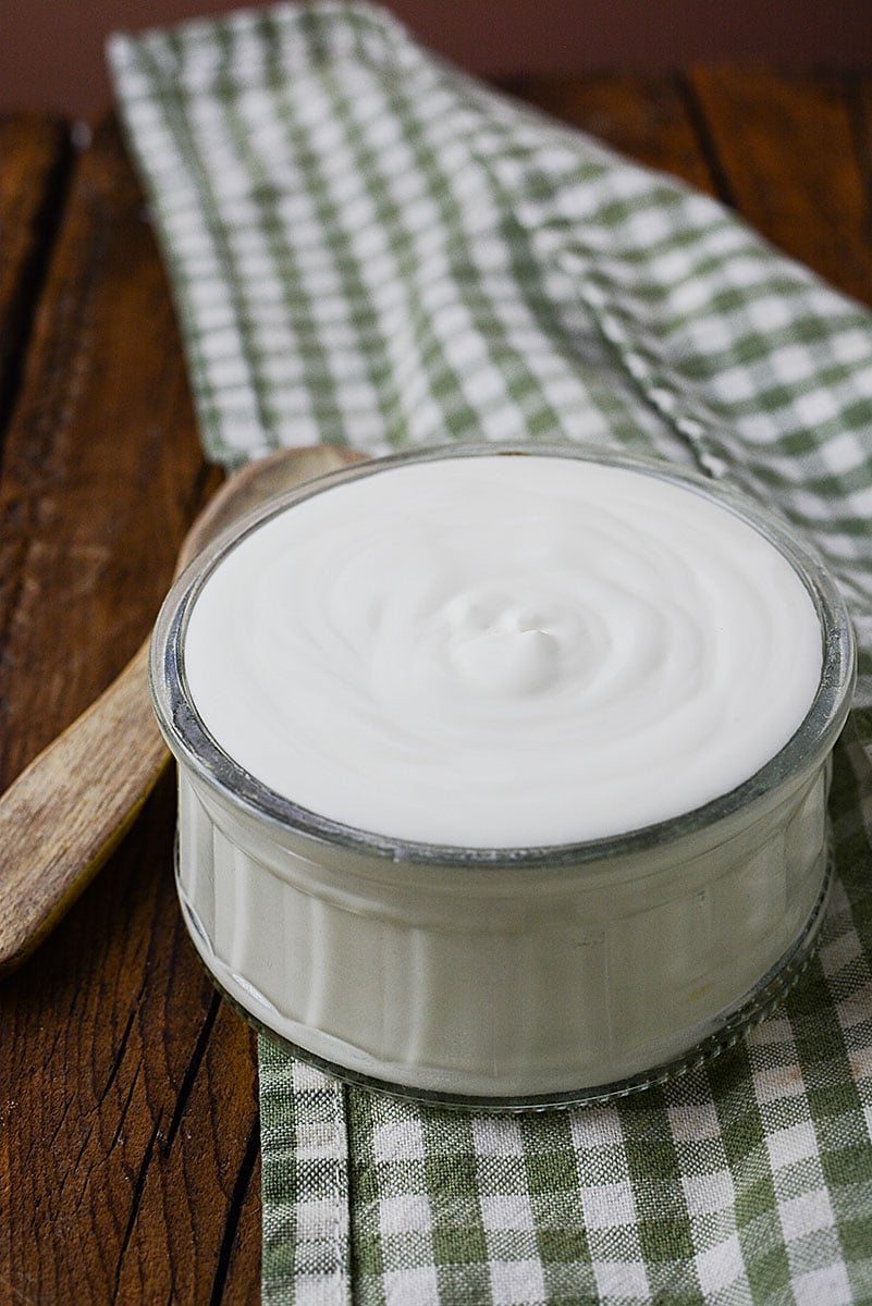 A small bowl of home made CREME FRAICHE sitting in a glass bowl with a wooden spoon next to it.