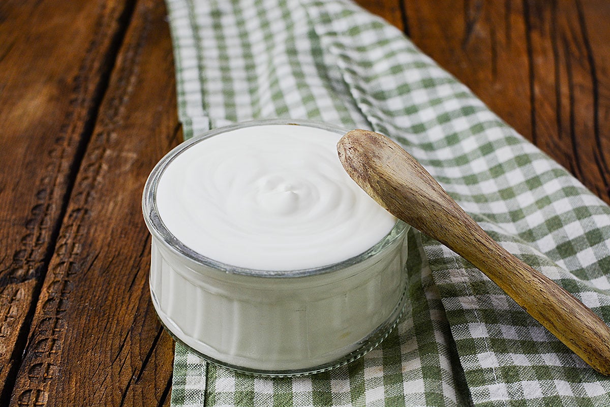 A small bowl of home made CREME FRAICHE sitting on a green and white checkered table cloth with a small wooden spoon next to it.