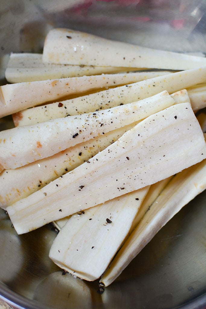 An image of fresh, peeled parsnips that are cut in half (lengthwise) seasoned with salt and pepper