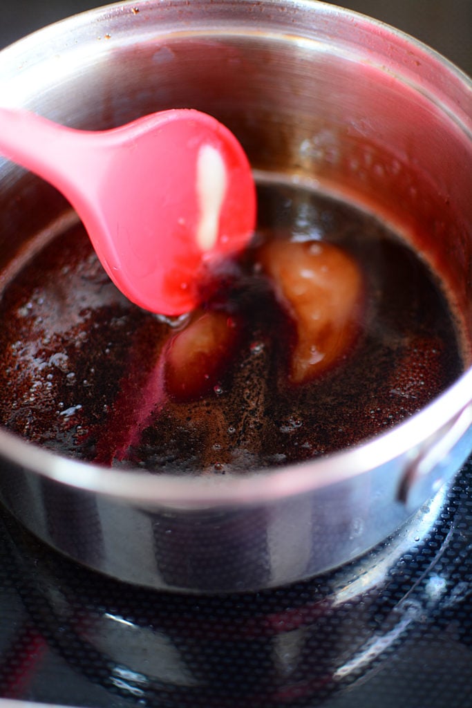 An image of pot with reduced pomegranate juice being mixed by a red ladle 