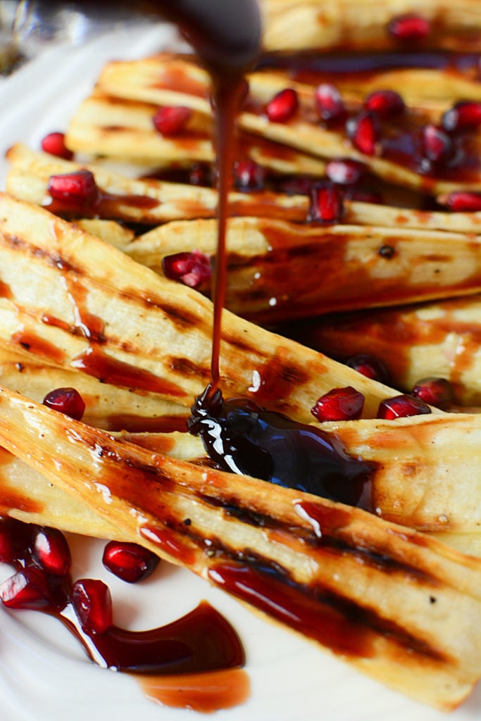 A close up image of Honey pomegranate juice being poured onto pieces of cooked parsnips with pomegranate seeds