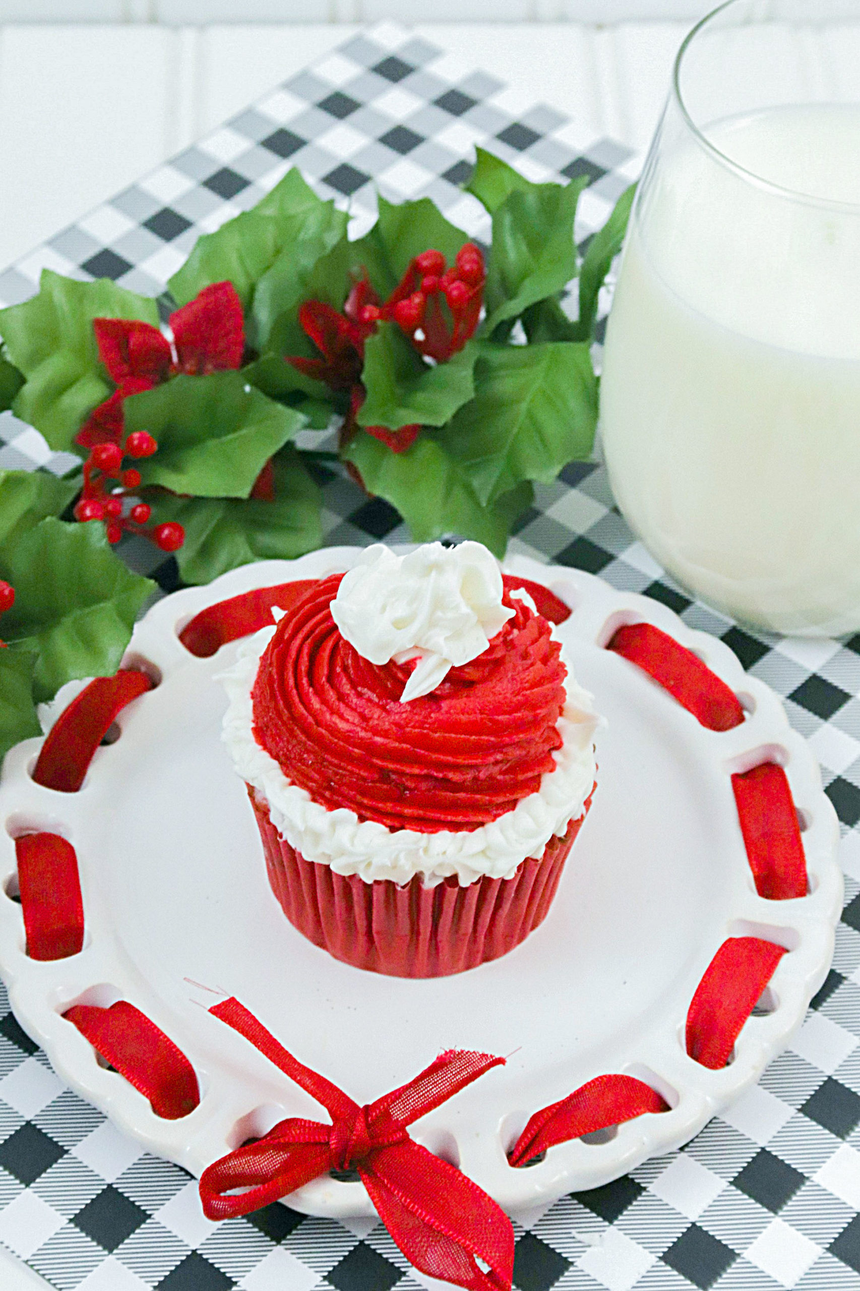 One Christmas Cupcake on a white plate with a big glass of milk on the right, and a sprig of holly on the top left.