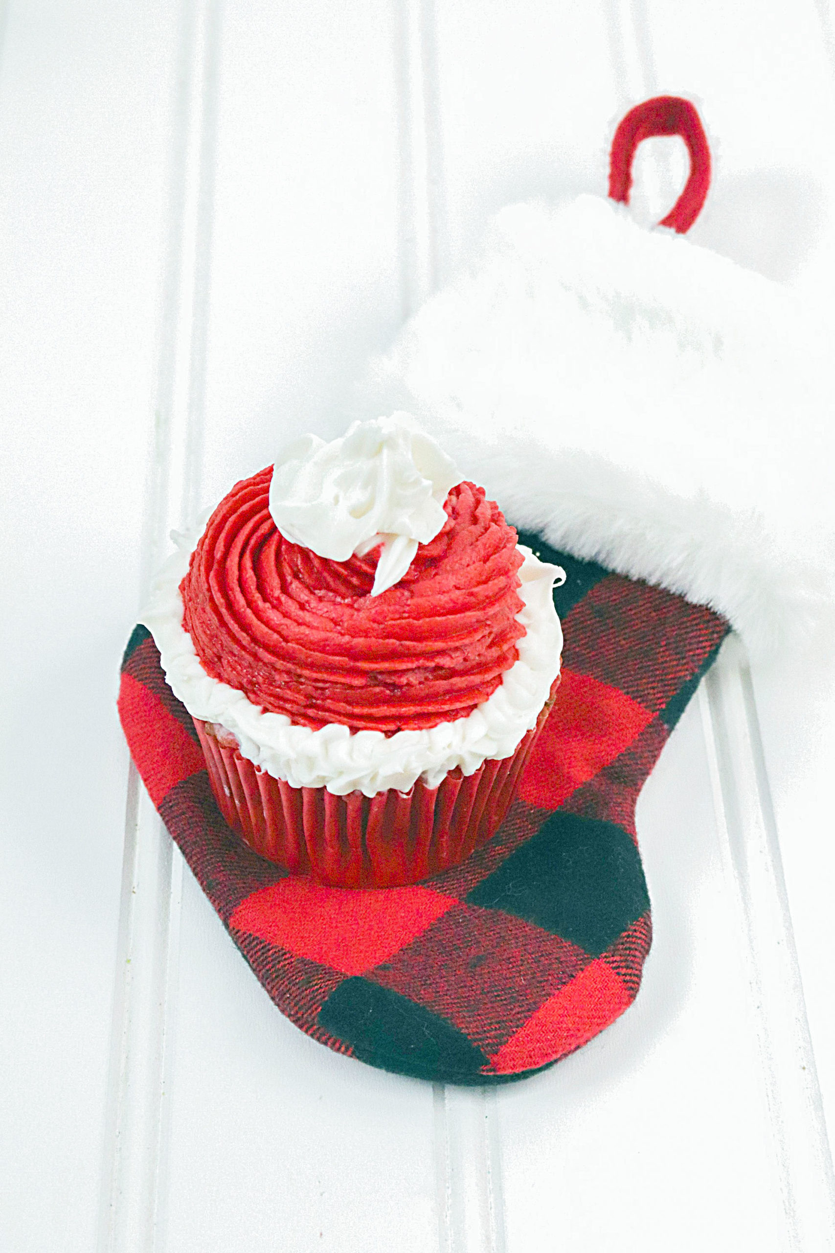 A santa's hat cupcake sitting on a red and white buffalo check stocking.