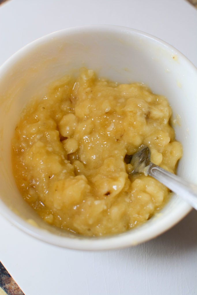 mashed over riped bananas in a white bowl with fork sticking in it