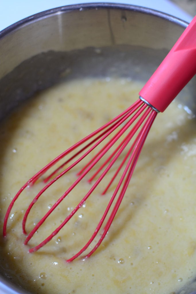 mashed over riped bananas with eggs in a silver mixing bowl with red whisk