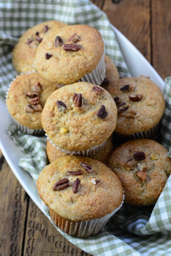 9 delicious banana muffins with pecans sitting on a white plate waiting to be devoured! 